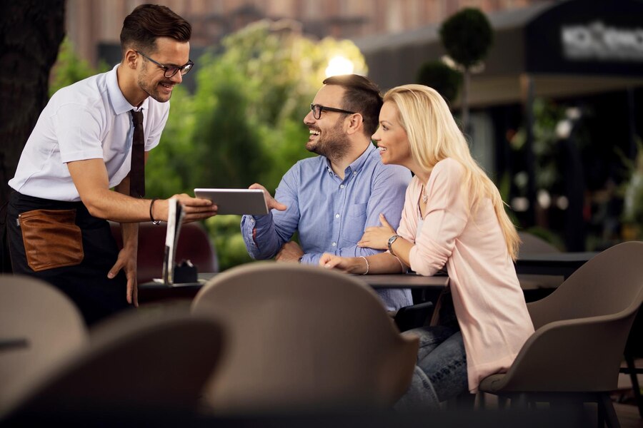 happy-couple-making-order-cafe-while-waiter-is-showing-them-menu-digital-table_637285-529